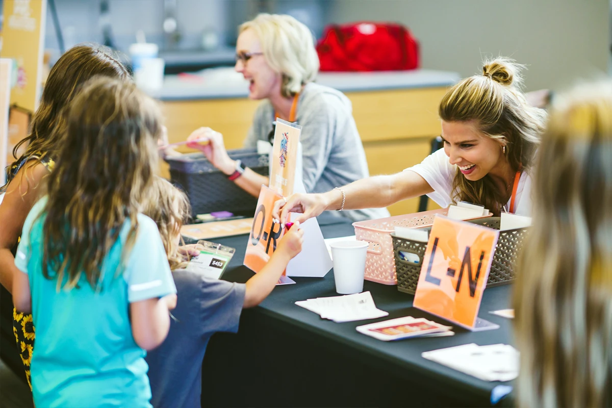 Women helping children at a registration table.